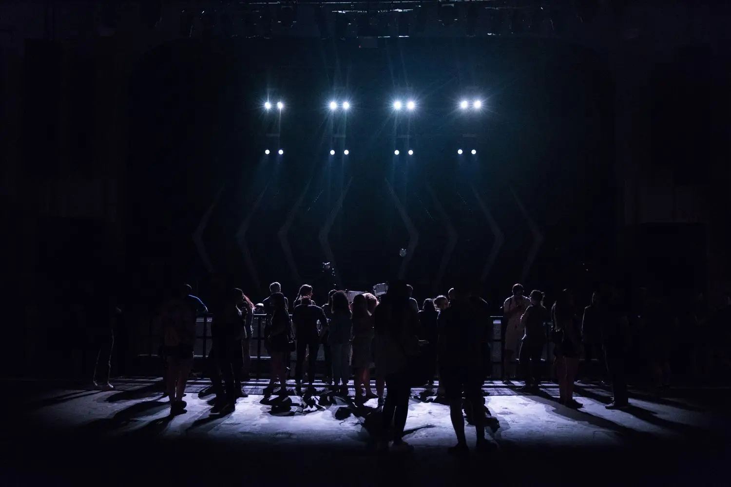 Actors gathered under focused stage lights during a theatre rehearsal