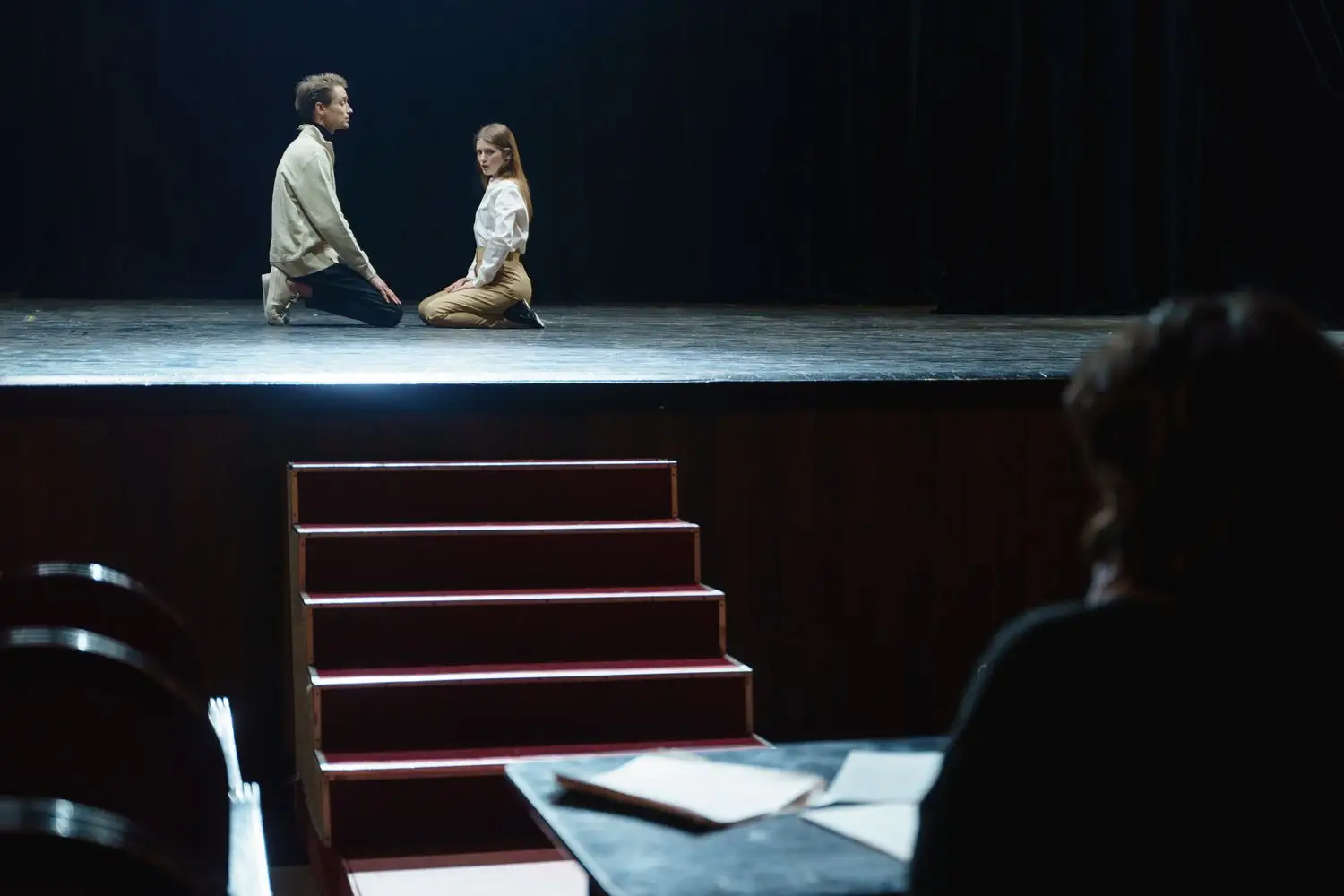 Two actors seated on a stage during rehearsal